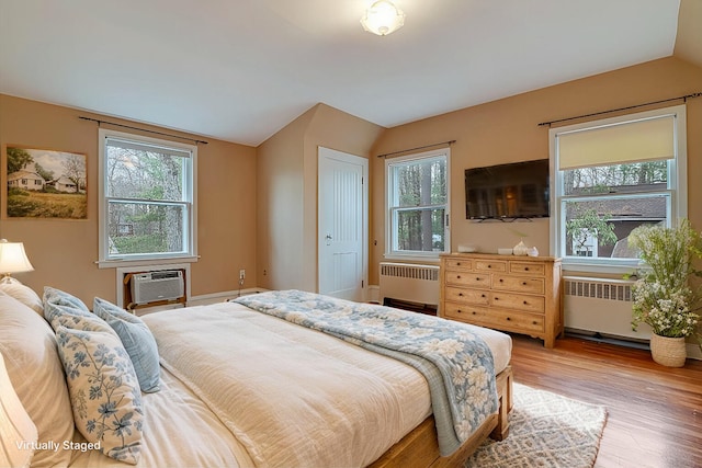 bedroom with radiator heating unit, light wood-style flooring, vaulted ceiling, and a wall mounted air conditioner