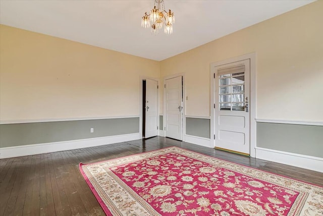 empty room featuring dark wood-style flooring, baseboards, and an inviting chandelier