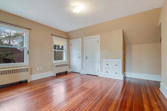 unfurnished bedroom featuring radiator heating unit, baseboards, wood finished floors, and lofted ceiling