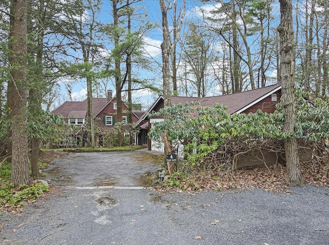 chalet / cabin with a chimney, a shingled roof, a garage, and aphalt driveway