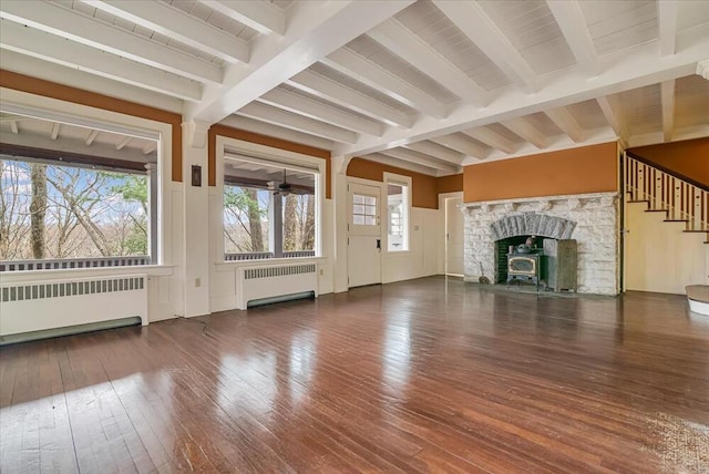 unfurnished living room featuring radiator, beam ceiling, hardwood / wood-style flooring, and stairs