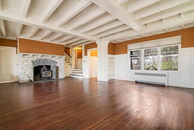 unfurnished living room featuring a decorative wall, hardwood / wood-style flooring, beamed ceiling, stairs, and radiator heating unit