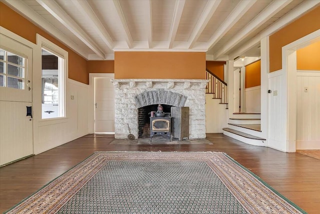 unfurnished living room with beamed ceiling, a wainscoted wall, stairway, and hardwood / wood-style flooring