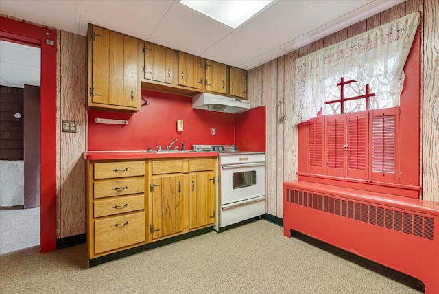kitchen with brown cabinetry, radiator heating unit, under cabinet range hood, a sink, and white range oven
