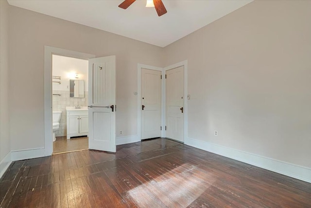 unfurnished bedroom with dark wood-style flooring, baseboards, ensuite bath, and a sink