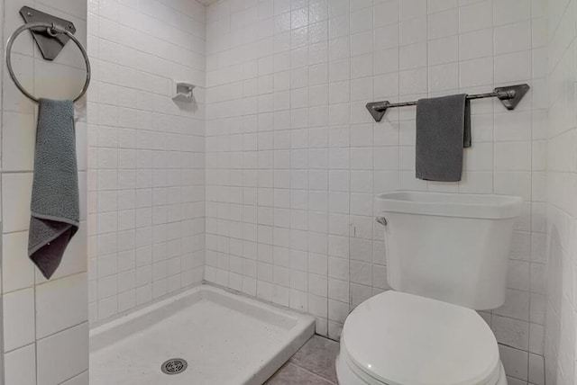 bathroom with tile walls, toilet, and a stall shower