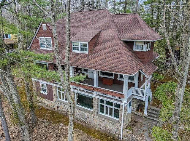back of property featuring a shingled roof, stone siding, and a chimney