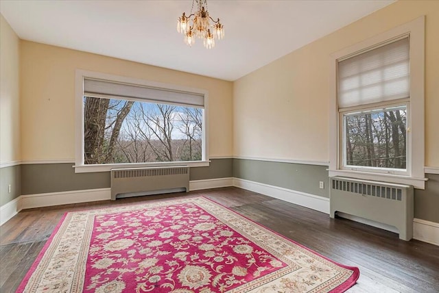 spare room featuring baseboards, radiator, a chandelier, and wood finished floors