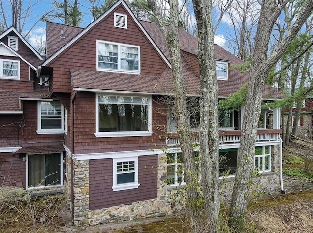 back of property featuring stone siding and a shingled roof