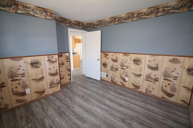 empty room with visible vents, wainscoting, and wood finished floors