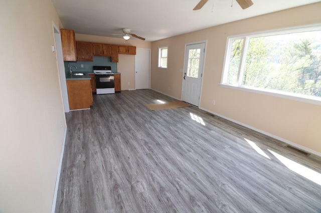 unfurnished living room with visible vents, a sink, wood finished floors, baseboards, and a ceiling fan