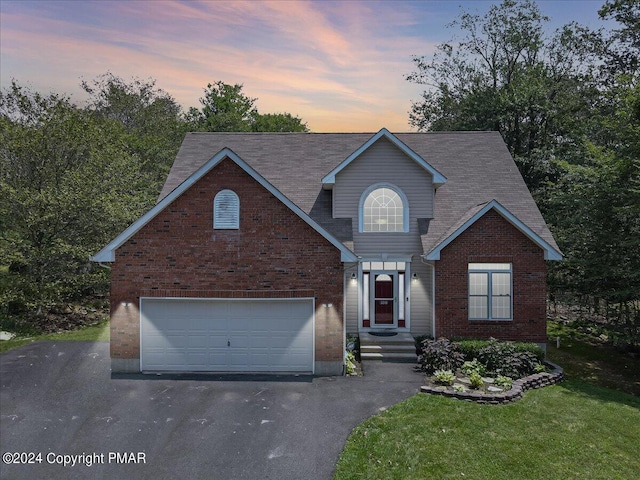 traditional-style house with aphalt driveway, brick siding, a garage, and a yard