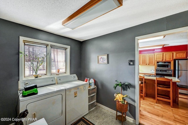 laundry room with a textured ceiling, laundry area, baseboards, light wood finished floors, and washer and clothes dryer