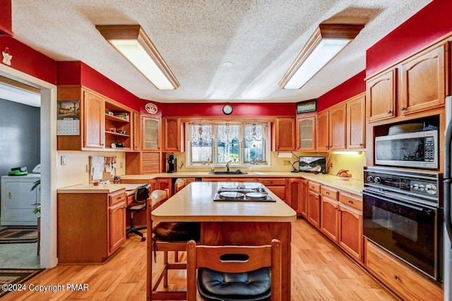 kitchen featuring electric cooktop, stainless steel microwave, light countertops, separate washer and dryer, and black oven