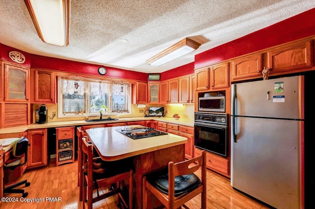 kitchen featuring light wood-type flooring, black appliances, glass insert cabinets, and light countertops