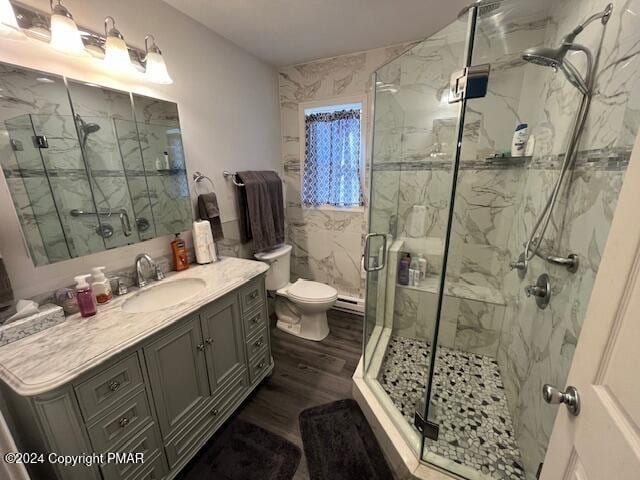 bathroom featuring toilet, wood finished floors, vanity, tile walls, and a marble finish shower