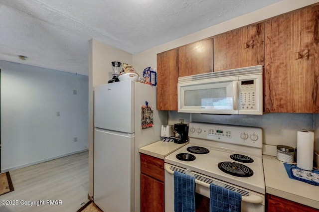 kitchen with light wood finished floors, white appliances, a textured ceiling, and light countertops