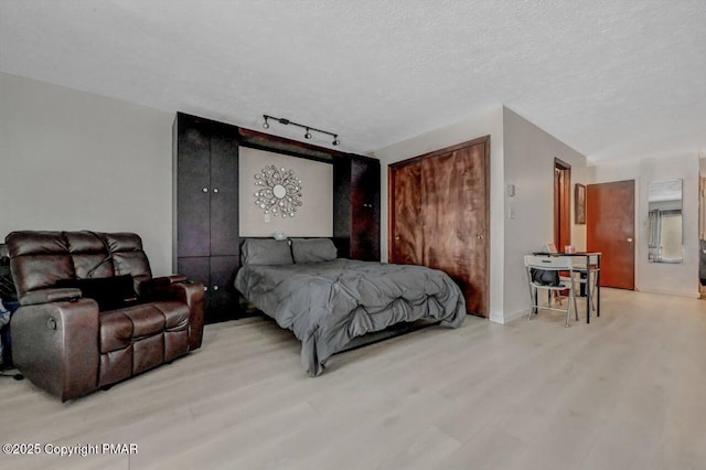 bedroom featuring rail lighting, a textured ceiling, and wood finished floors