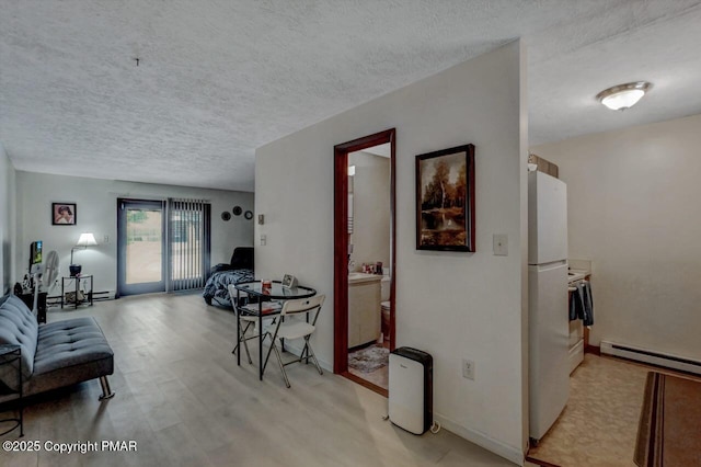 living area with a textured ceiling, a baseboard heating unit, and light wood-style floors