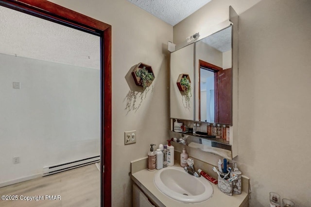 bathroom with a baseboard heating unit, wood finished floors, vanity, and a textured ceiling