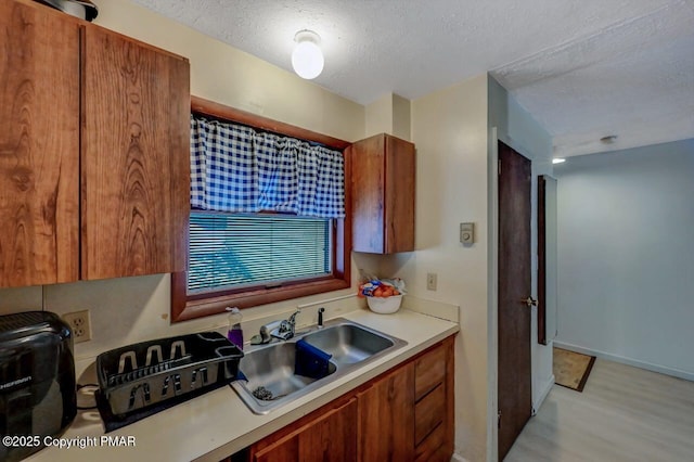 kitchen with light wood-type flooring, light countertops, brown cabinets, a textured ceiling, and a sink