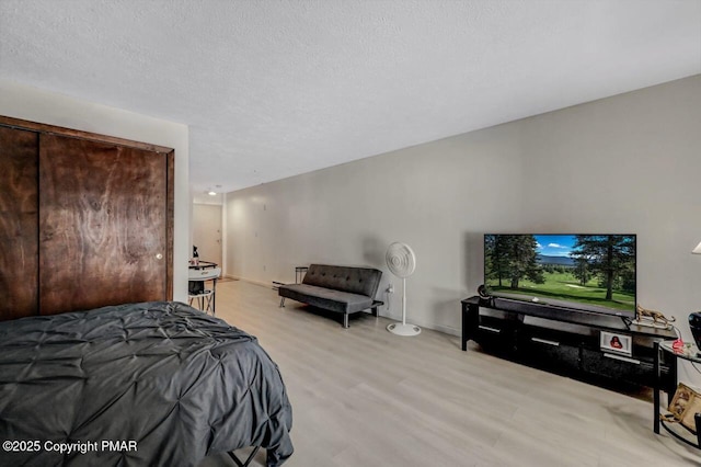 bedroom featuring baseboards, light wood-style floors, and a textured ceiling