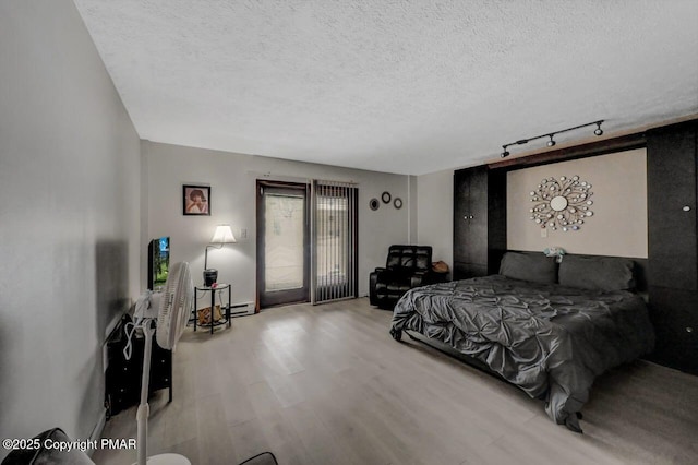 bedroom with track lighting, access to outside, wood finished floors, and a textured ceiling