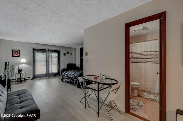 interior space with light wood-style floors, access to exterior, ensuite bathroom, and a textured ceiling