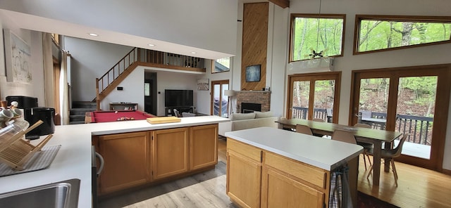 kitchen with a high ceiling, a brick fireplace, light wood-style flooring, light countertops, and a peninsula