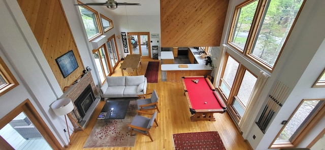 playroom featuring a towering ceiling, wood finished floors, a fireplace with raised hearth, ceiling fan, and pool table