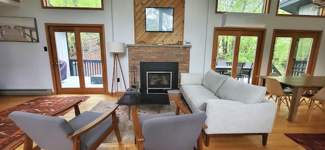 living room with a high ceiling, wood finished floors, a baseboard heating unit, and a brick fireplace
