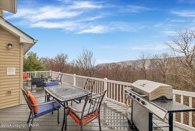 wooden deck featuring a forest view, grilling area, and outdoor dining space