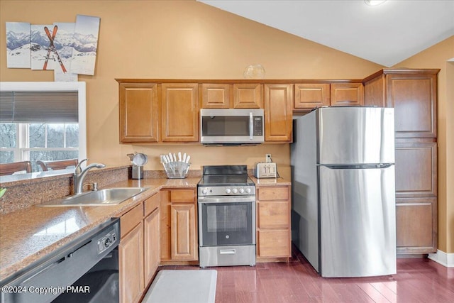 kitchen featuring light stone counters, lofted ceiling, a sink, stainless steel appliances, and dark wood-type flooring