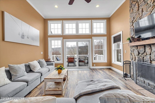 living room featuring a stone fireplace, crown molding, baseboards, and wood finished floors