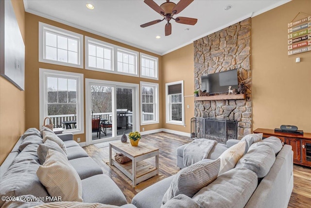 living area featuring a stone fireplace, a healthy amount of sunlight, crown molding, and wood finished floors