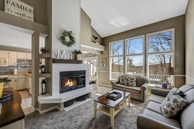 living area with light tile patterned flooring, light colored carpet, high vaulted ceiling, and a tile fireplace
