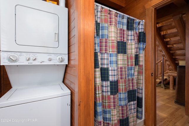 laundry area with laundry area, wooden walls, stacked washing maching and dryer, and wood finished floors