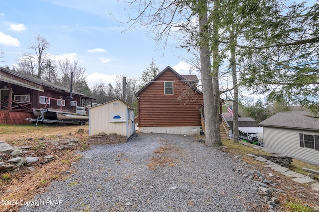 view of side of home with driveway, a storage shed, log siding, an outbuilding, and crawl space