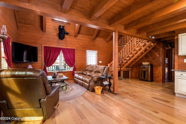 living room featuring light wood-type flooring, beam ceiling, wooden walls, and stairs