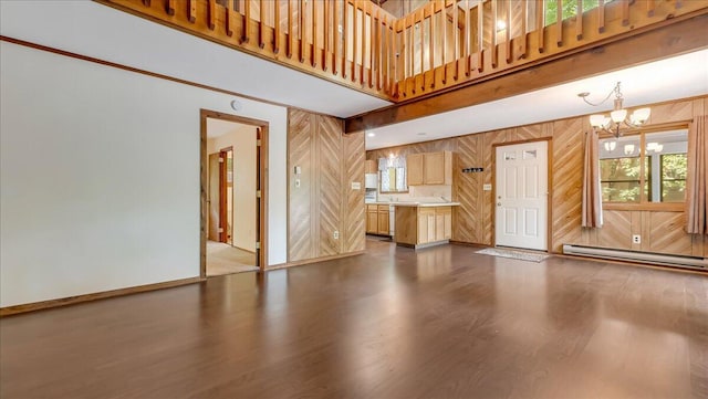 5913 NE Decker Rd NE, Bushkill, PA 18324 - unfurnished living room featuring baseboard heating, a chandelier, dark wood finished floors, wooden walls, and healthy amount of natural light