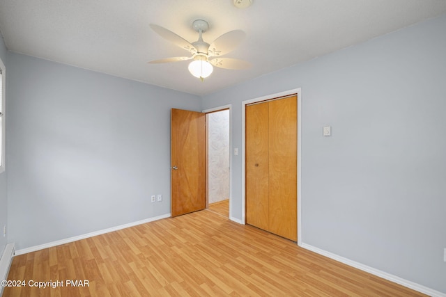 unfurnished bedroom with baseboard heating, a closet, baseboards, and wood finished floors