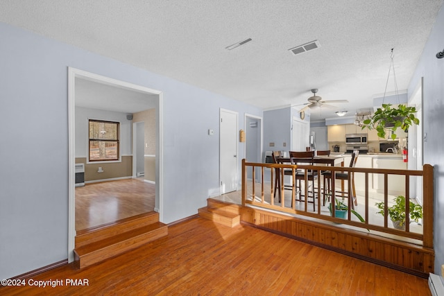 interior space with a baseboard radiator, a textured ceiling, visible vents, and wood finished floors