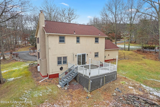 back of property with a deck, roof with shingles, a chimney, and a lawn