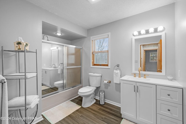 bathroom with toilet, a textured ceiling, vanity, wood finished floors, and baseboards