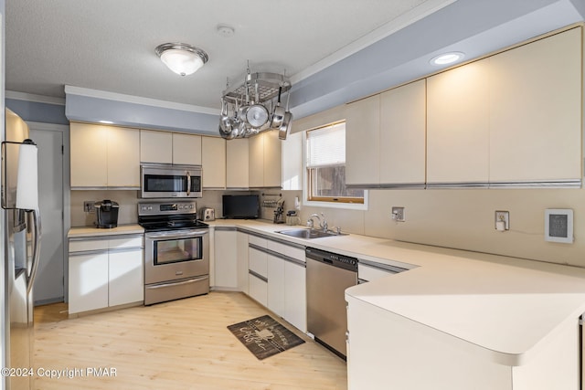 kitchen with a peninsula, a sink, light countertops, appliances with stainless steel finishes, and crown molding