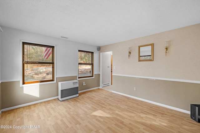 empty room with heating unit, visible vents, baseboard heating, wood finished floors, and baseboards