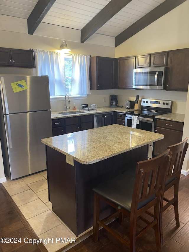 kitchen with vaulted ceiling with beams, a breakfast bar area, stainless steel appliances, a sink, and light stone countertops