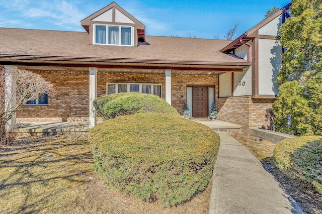 view of front of home featuring brick siding and roof with shingles