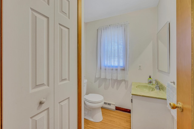 half bathroom with vanity, wood finished floors, baseboards, toilet, and baseboard heating