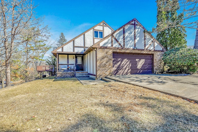 tudor house featuring driveway, covered porch, a front yard, a garage, and brick siding